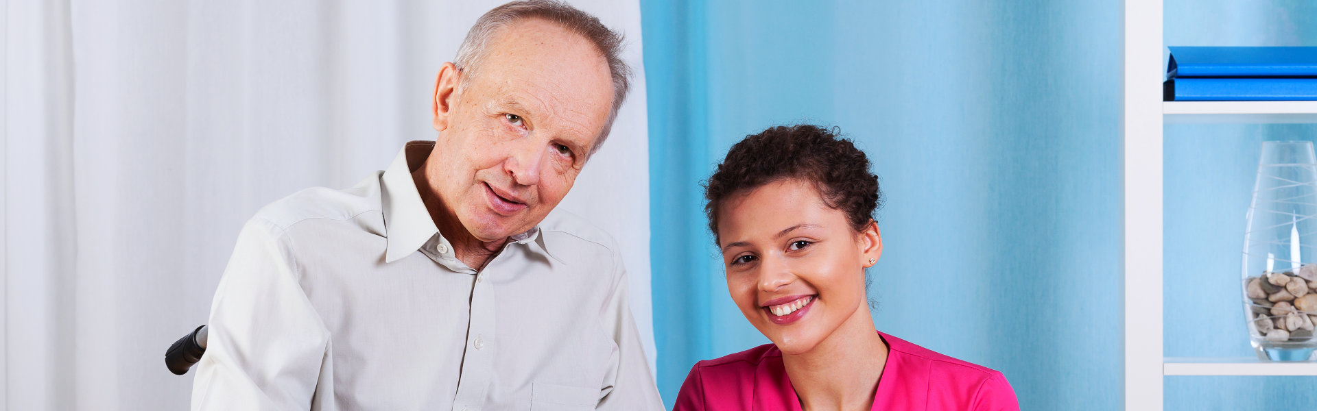 elderly man in a wheelchair and his aide smiling